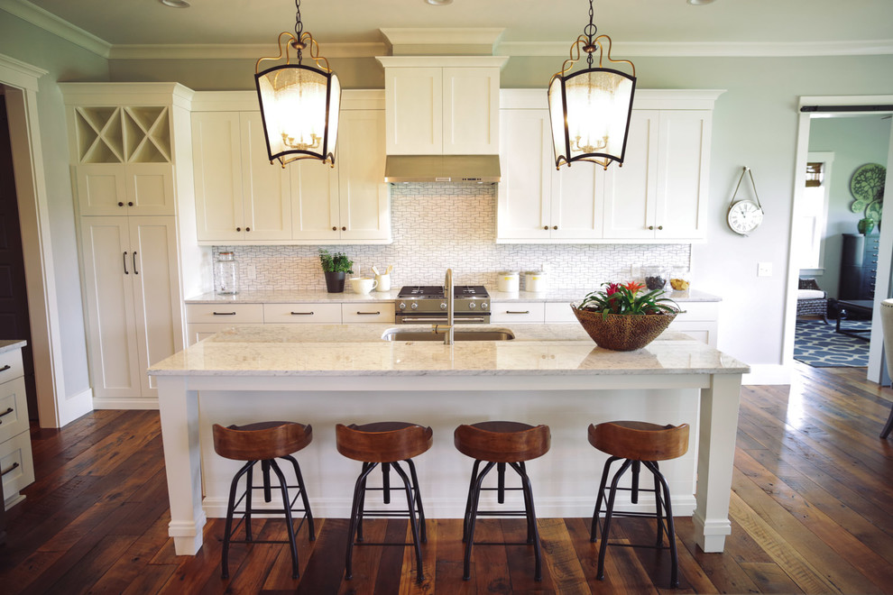 Foto på ett funkis kök, med en undermonterad diskho, vita skåp, marmorbänkskiva, vitt stänkskydd, rostfria vitvaror, mellanmörkt trägolv och en köksö
