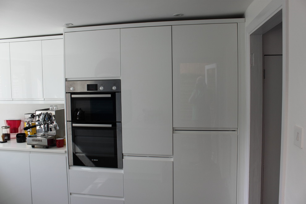 Photo of a medium sized contemporary u-shaped enclosed kitchen in London with a submerged sink, flat-panel cabinets, white cabinets, engineered stone countertops, blue splashback, glass sheet splashback, black appliances, lino flooring and no island.