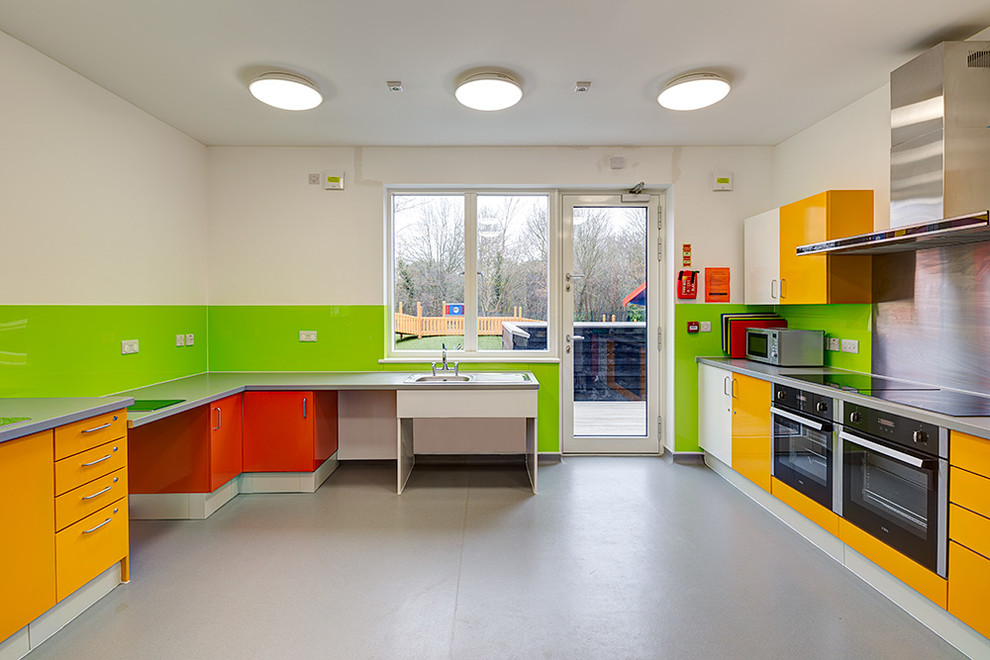 Источник вдохновения для домашнего уюта: большая кухня в современном стиле с монолитной мойкой, плоскими фасадами, желтыми фасадами, зеленым фартуком, черной техникой и полом из линолеума