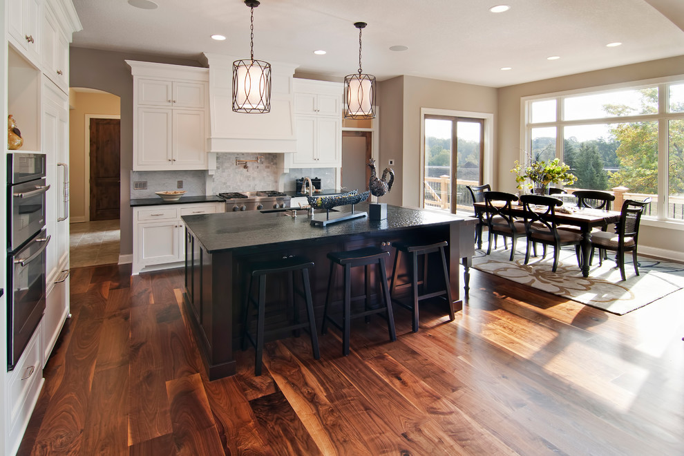 Inspiration for a transitional brown floor eat-in kitchen remodel in Minneapolis with recessed-panel cabinets, white cabinets, white backsplash, stainless steel appliances, granite countertops and stone tile backsplash