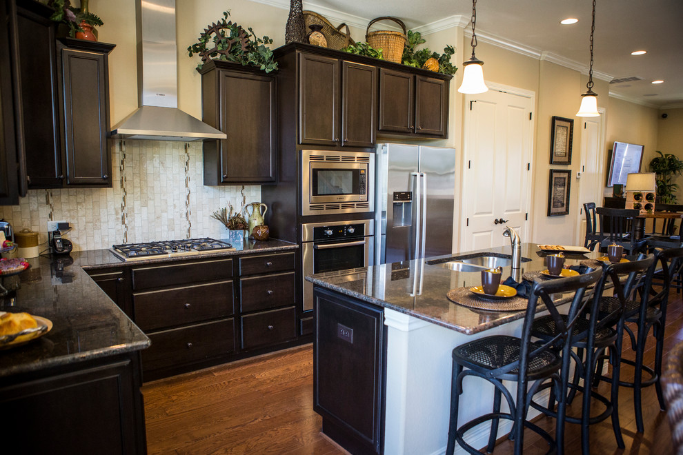 Exempel på ett mellanstort klassiskt kök, med en dubbel diskho, luckor med infälld panel, svarta skåp, granitbänkskiva, beige stänkskydd, stänkskydd i keramik, rostfria vitvaror, mellanmörkt trägolv och en köksö