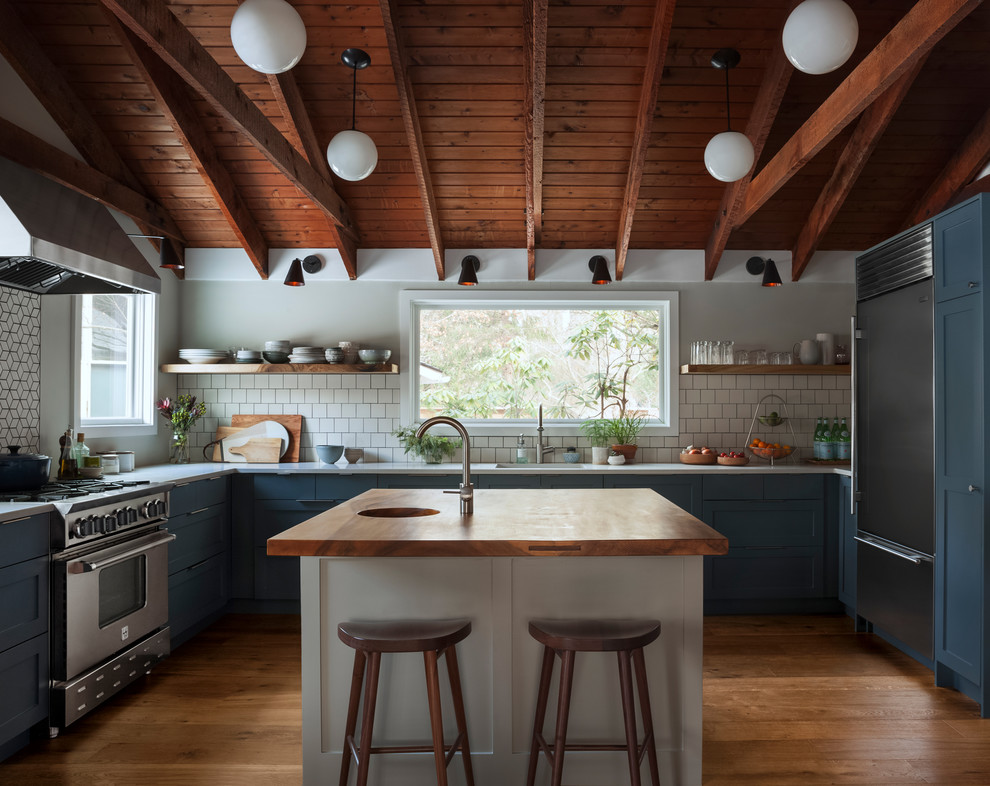 Inspiration for a classic u-shaped kitchen in Other with an integrated sink, shaker cabinets, blue cabinets, wood worktops, white splashback, stainless steel appliances, medium hardwood flooring, an island, brown floors and brown worktops.