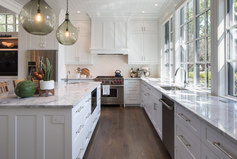 Photo of a large rural l-shaped kitchen in Calgary with white cabinets, white splashback, stainless steel appliances, dark hardwood flooring, an island, brown floors, a built-in sink, quartz worktops, porcelain splashback and grey worktops.