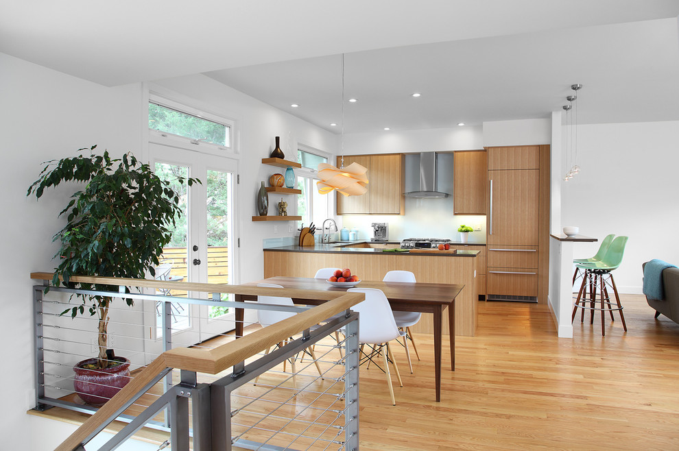 Medium sized retro u-shaped open plan kitchen in Denver with a submerged sink, flat-panel cabinets, light wood cabinets, white splashback, integrated appliances and light hardwood flooring.