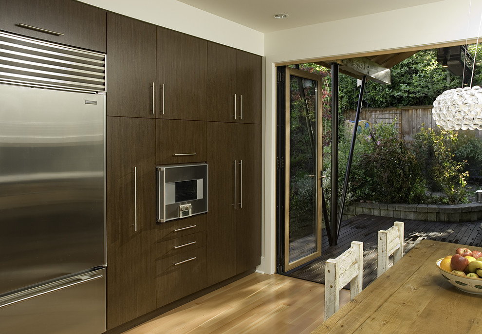 Diseño de cocina actual con electrodomésticos de acero inoxidable, armarios con paneles lisos y puertas de armario de madera en tonos medios