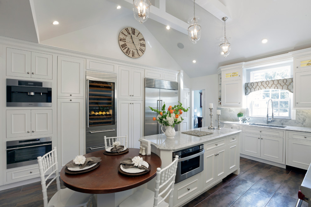 Bild på ett stort lantligt kök, med en undermonterad diskho, luckor med infälld panel, vita skåp, vitt stänkskydd, rostfria vitvaror, en köksö och klinkergolv i porslin