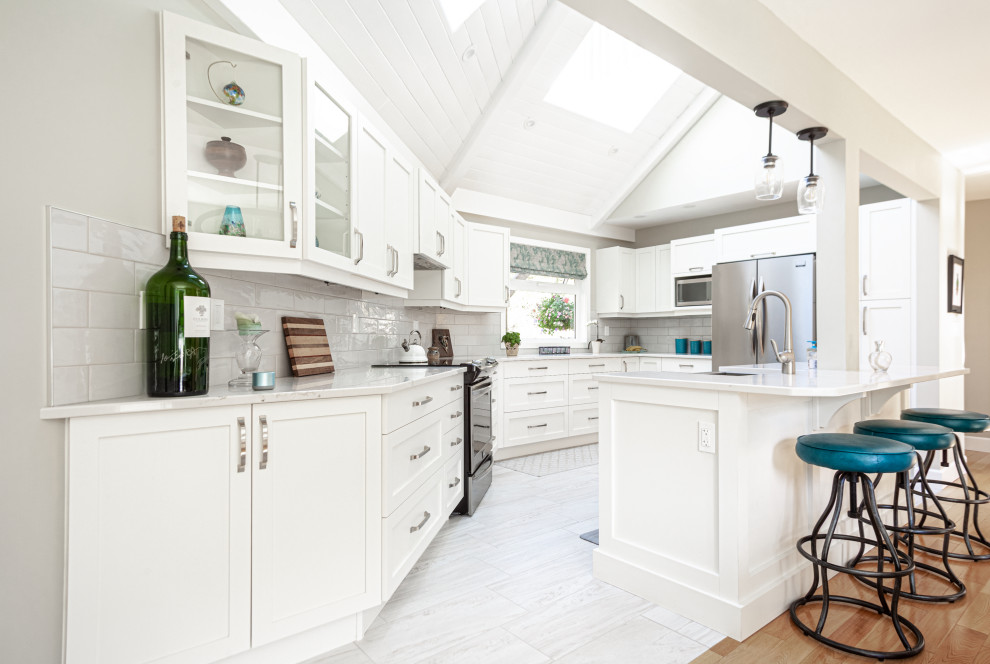 Inspiration for a medium sized classic u-shaped kitchen/diner in Vancouver with a belfast sink, shaker cabinets, white cabinets, engineered stone countertops, grey splashback, ceramic splashback, stainless steel appliances, laminate floors, an island, beige floors and white worktops.