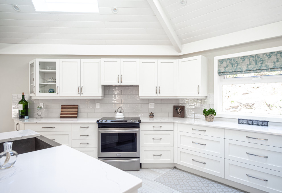 Design ideas for a medium sized classic u-shaped kitchen/diner in Vancouver with a belfast sink, shaker cabinets, white cabinets, engineered stone countertops, grey splashback, ceramic splashback, stainless steel appliances, laminate floors, an island, beige floors and white worktops.