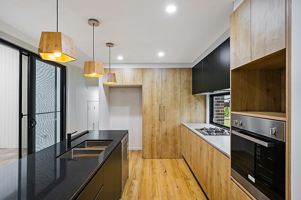 Inspiration for a contemporary l-shaped open plan kitchen in Brisbane with a submerged sink, light wood cabinets, window splashback, stainless steel appliances, light hardwood flooring and an island.