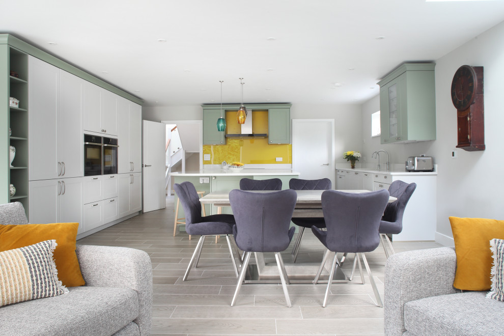 Offene Moderne Küche in U-Form mit Schrankfronten im Shaker-Stil, grünen Schränken, Küchenrückwand in Gelb, Glasrückwand, Küchengeräten aus Edelstahl, Kücheninsel, grauem Boden und weißer Arbeitsplatte in Buckinghamshire