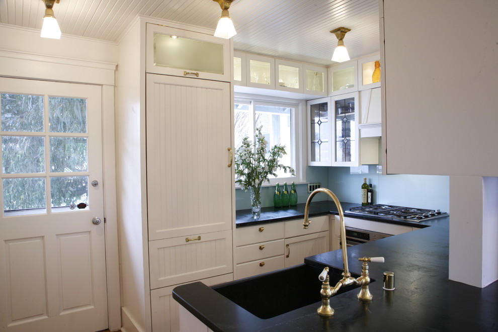 Kitchen - traditional u-shaped kitchen idea in Los Angeles with a farmhouse sink, white cabinets, soapstone countertops, blue backsplash, glass sheet backsplash and paneled appliances