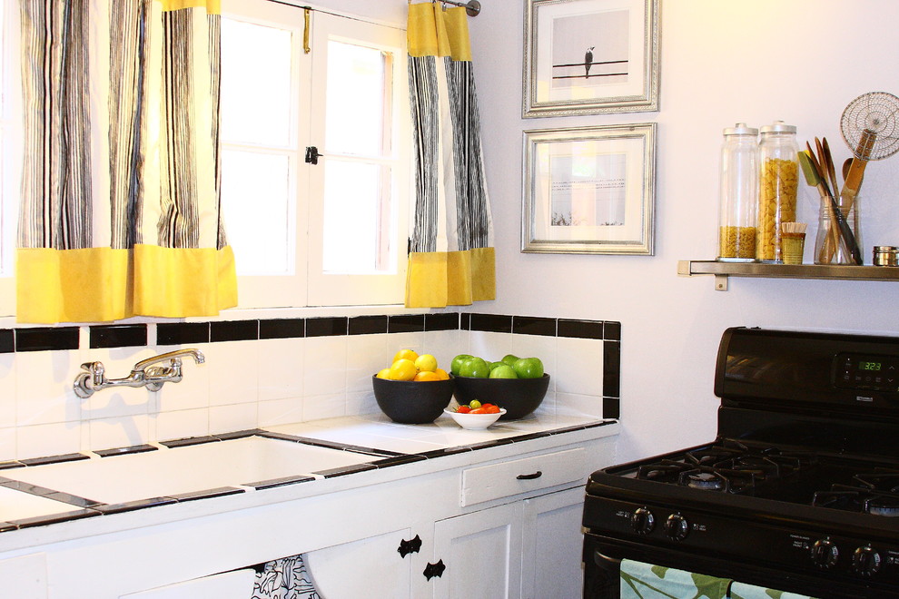 Modelo de cocina clásica con armarios estilo shaker, puertas de armario blancas, encimera de azulejos, salpicadero multicolor y electrodomésticos negros