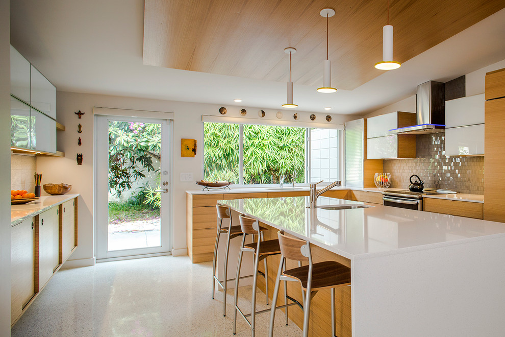 Exemple d'une cuisine rétro en L et bois clair avec un placard à porte plane, une crédence grise, une crédence en carreau de verre, sol en béton ciré, îlot, un évier encastré et un sol blanc.