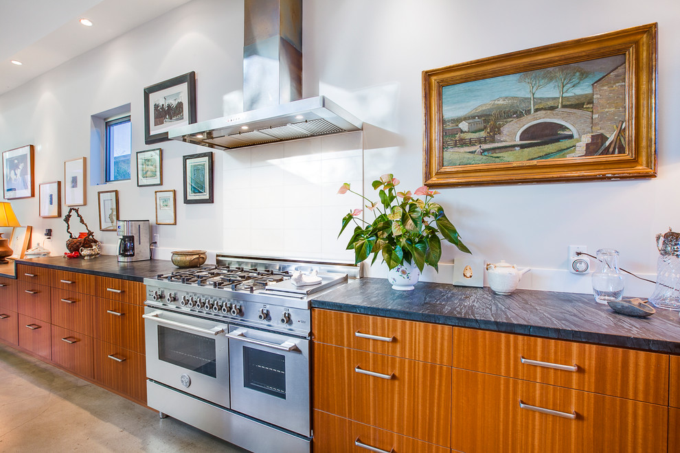Imagen de cocina lineal actual con armarios con paneles lisos, puertas de armario de madera clara, salpicadero blanco y electrodomésticos de acero inoxidable