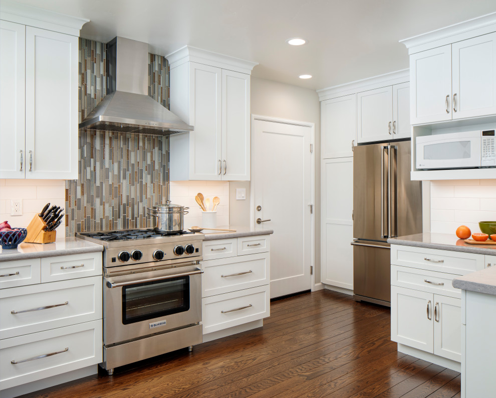 Exempel på ett avskilt, mellanstort klassiskt grå grått u-kök, med skåp i shakerstil, vita skåp, bänkskiva i kvarts, flerfärgad stänkskydd, stänkskydd i keramik, rostfria vitvaror, mellanmörkt trägolv och brunt golv