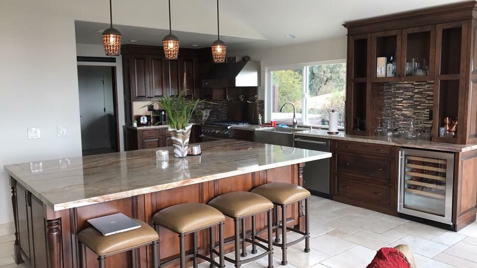 Example of a large island style l-shaped travertine floor and beige floor eat-in kitchen design in Los Angeles with raised-panel cabinets, dark wood cabinets, quartzite countertops, brown backsplash, stainless steel appliances, an island, a farmhouse sink and matchstick tile backsplash
