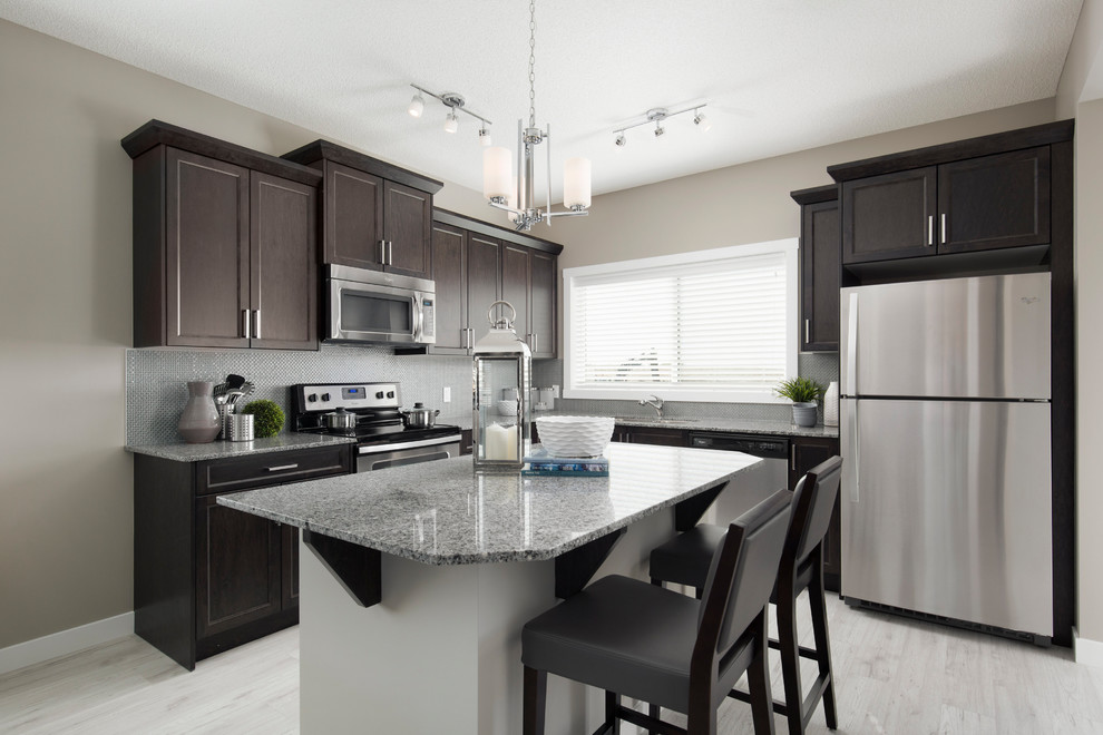 Mid-sized trendy l-shaped laminate floor and beige floor open concept kitchen photo in Calgary with an undermount sink, shaker cabinets, medium tone wood cabinets, granite countertops, multicolored backsplash, mosaic tile backsplash, stainless steel appliances and an island
