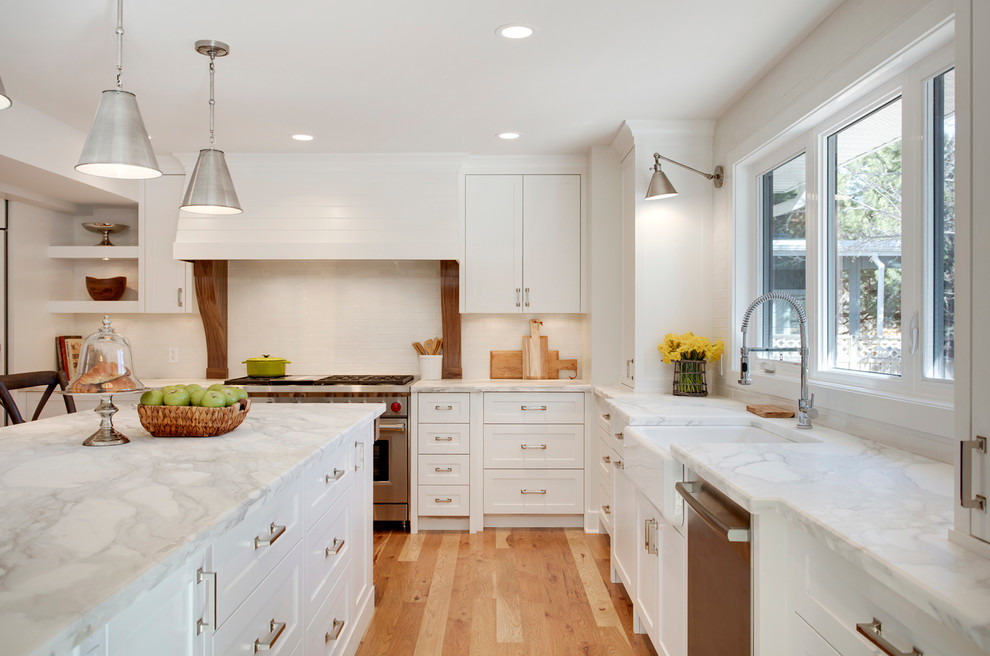 Cottage medium tone wood floor kitchen photo in Calgary with a farmhouse sink, shaker cabinets, white cabinets, white backsplash, stainless steel appliances and an island
