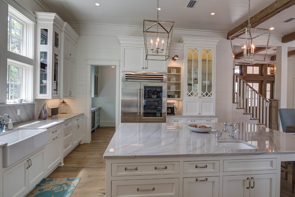 Example of a large beach style u-shaped light wood floor and beige floor open concept kitchen design in Atlanta with a farmhouse sink, recessed-panel cabinets, white cabinets, marble countertops, gray backsplash, glass tile backsplash, stainless steel appliances and an island