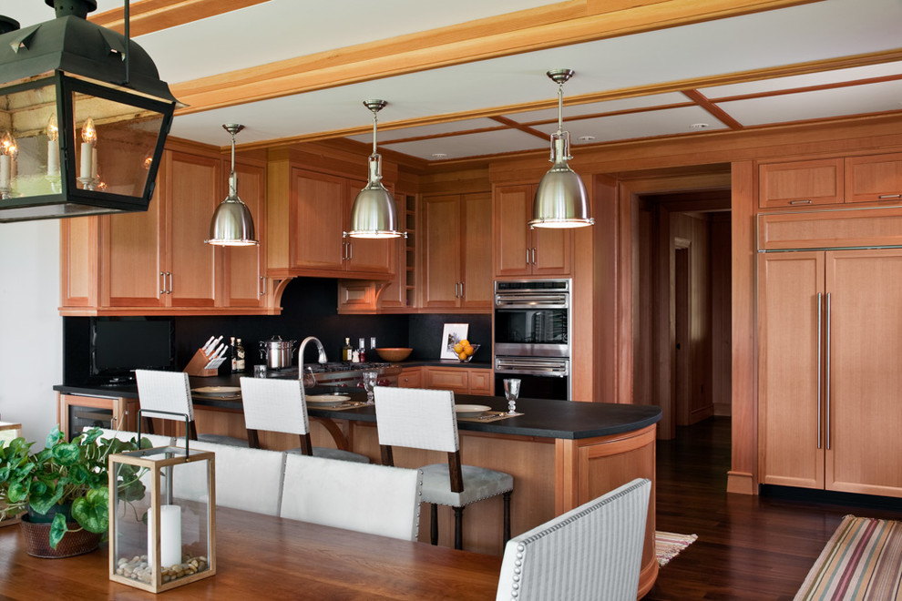 Example of a large arts and crafts u-shaped dark wood floor eat-in kitchen design in Burlington with a farmhouse sink, recessed-panel cabinets, medium tone wood cabinets, black backsplash, stone slab backsplash, stainless steel appliances and a peninsula