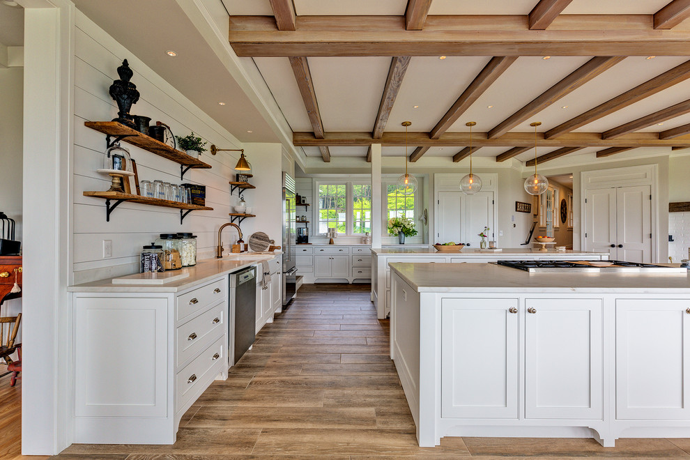 Inspiration for a farmhouse ceramic tile and brown floor eat-in kitchen remodel in Burlington with a farmhouse sink, shaker cabinets, white cabinets, marble countertops, white backsplash, wood backsplash, stainless steel appliances, two islands and white countertops