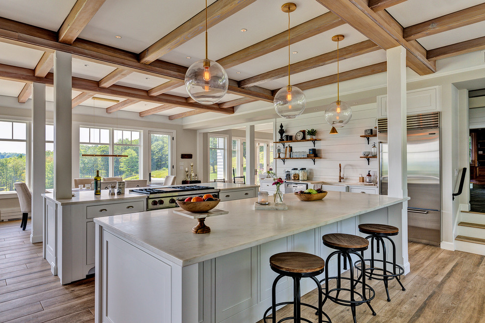 Bild på ett lantligt vit vitt kök och matrum, med en rustik diskho, skåp i shakerstil, vita skåp, marmorbänkskiva, vitt stänkskydd, stänkskydd i trä, rostfria vitvaror, flera köksöar, brunt golv och klinkergolv i keramik