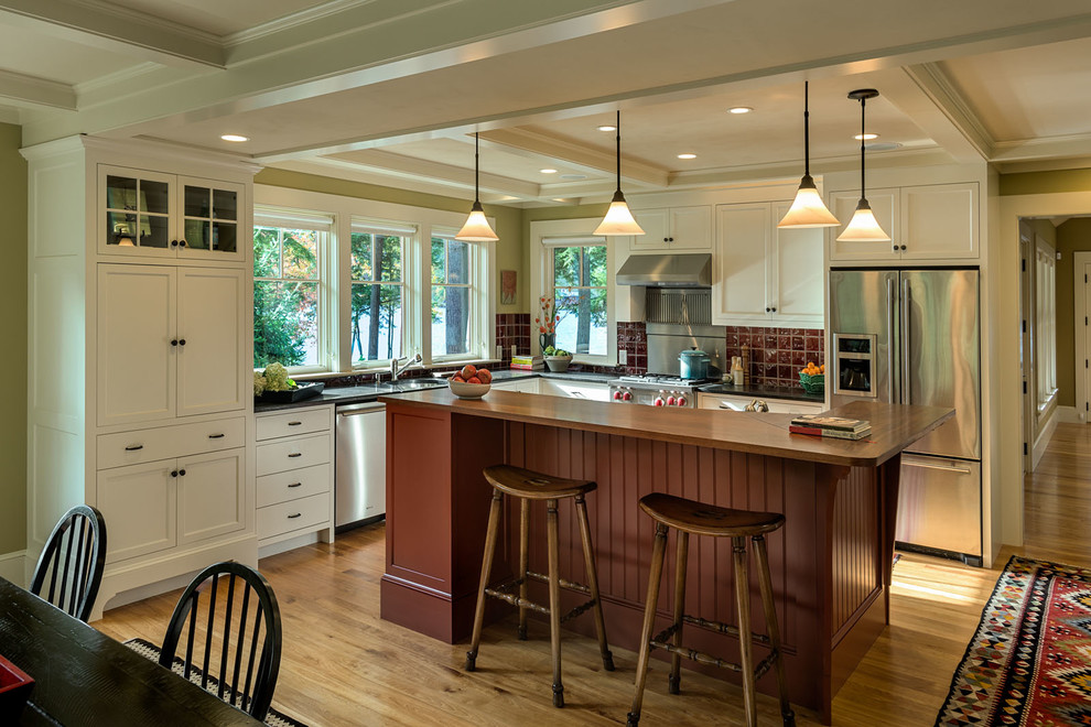 Klassische Küche mit Schrankfronten mit vertiefter Füllung, weißen Schränken, Küchenrückwand in Rot, Küchengeräten aus Edelstahl, braunem Holzboden und Kücheninsel in Burlington
