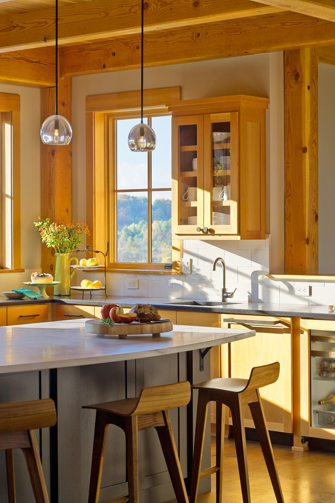 Rustik inredning av ett l-kök, med luckor med glaspanel, skåp i ljust trä, vitt stänkskydd och en köksö