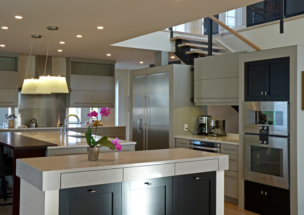 Bild på ett stort funkis kök, med en undermonterad diskho, grå skåp, bänkskiva i kvarts, rostfria vitvaror, ljust trägolv och flera köksöar