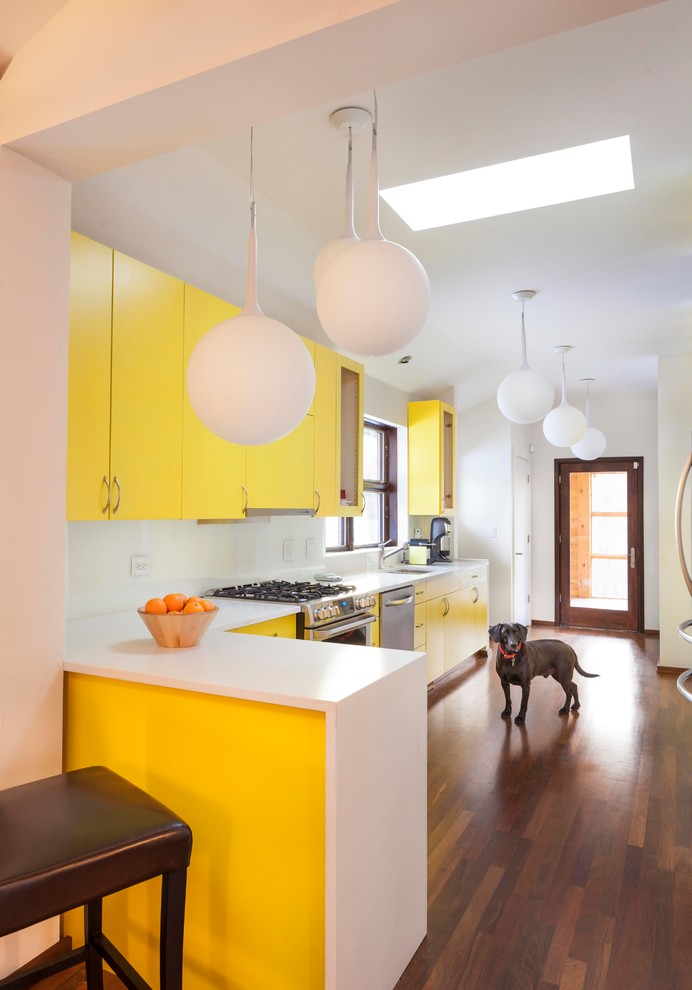 Moderne Schmale Küche in L-Form mit Unterbauwaschbecken, flächenbündigen Schrankfronten, gelben Schränken, Küchenrückwand in Weiß, Küchengeräten aus Edelstahl, dunklem Holzboden, Halbinsel und weißer Arbeitsplatte in Chicago