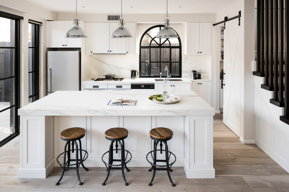 Large urban galley medium tone wood floor and gray floor open concept kitchen photo in Melbourne with a double-bowl sink, recessed-panel cabinets, white cabinets, quartz countertops, white backsplash, marble backsplash, white appliances and an island