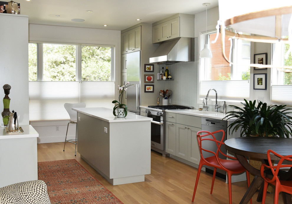This is an example of a small traditional galley kitchen/diner in Denver with brown floors, grey cabinets, grey splashback, stainless steel appliances, an island, recessed-panel cabinets, mosaic tiled splashback, medium hardwood flooring and white worktops.