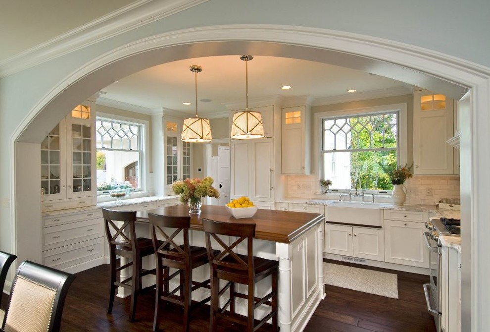 Exempel på ett klassiskt kök, med en rustik diskho, luckor med glaspanel, vita skåp, fönster som stänkskydd, rostfria vitvaror, mörkt trägolv, en köksö och brunt golv