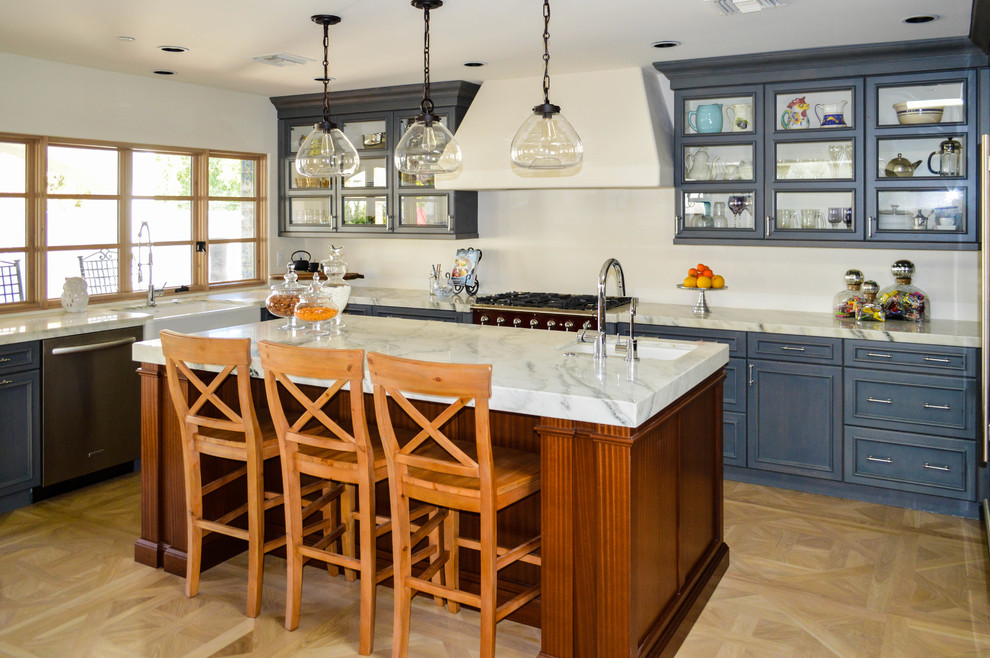 Large elegant u-shaped light wood floor eat-in kitchen photo in Phoenix with a farmhouse sink, glass-front cabinets, blue cabinets, marble countertops, stainless steel appliances and an island