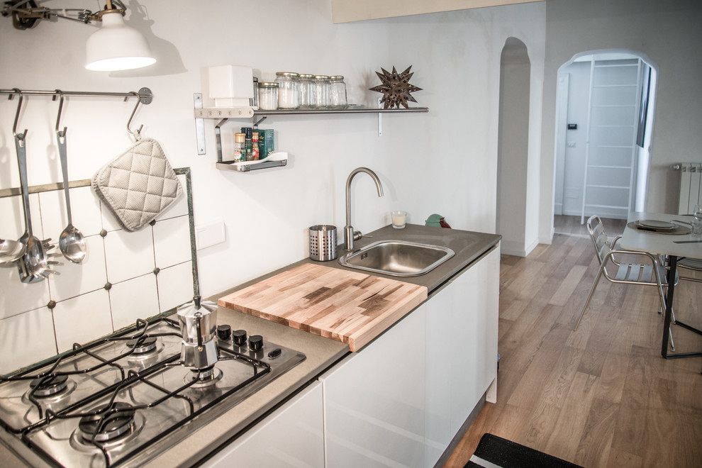 Small contemporary single-wall enclosed kitchen in Turin with no island, flat-panel cabinets, white cabinets, limestone worktops, white splashback, ceramic splashback, stainless steel appliances, a single-bowl sink and medium hardwood flooring.