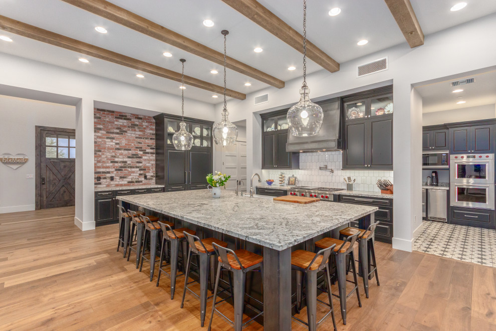 Transitional u-shaped medium tone wood floor, brown floor and exposed beam open concept kitchen photo in Phoenix with an undermount sink, raised-panel cabinets, gray cabinets, white backsplash, stainless steel appliances and an island