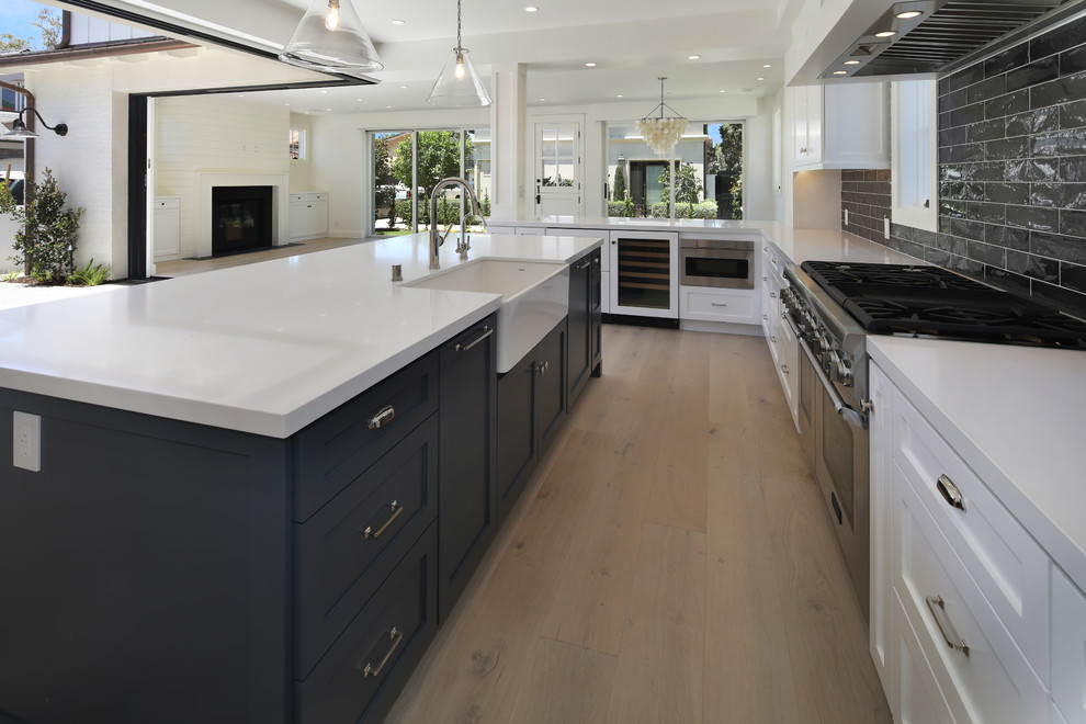 Large trendy l-shaped light wood floor and beige floor open concept kitchen photo in Orange County with a farmhouse sink, shaker cabinets, white cabinets, quartz countertops, black backsplash, subway tile backsplash, paneled appliances, an island and white countertops