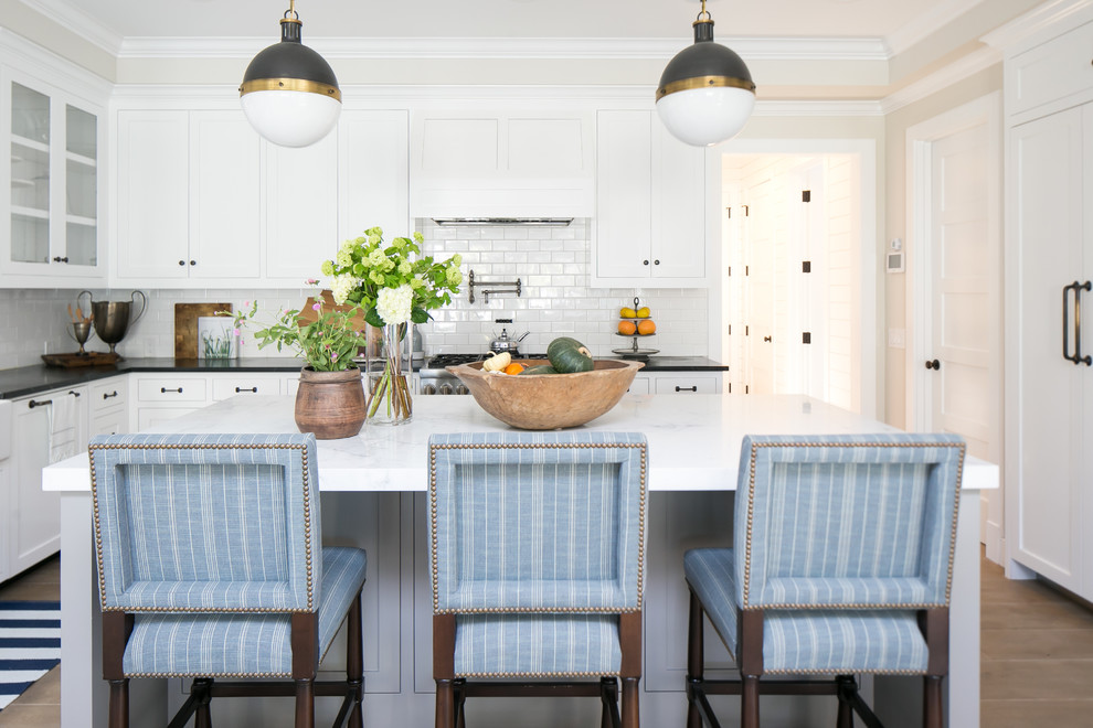Inspiration for a coastal l-shaped enclosed kitchen in Orange County with shaker cabinets, white cabinets, white splashback, metro tiled splashback, an island and beige floors.