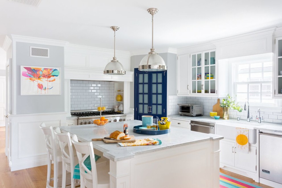 Example of an eclectic l-shaped light wood floor eat-in kitchen design in Los Angeles with a farmhouse sink, beaded inset cabinets, white cabinets, marble countertops, white backsplash, subway tile backsplash, stainless steel appliances and an island
