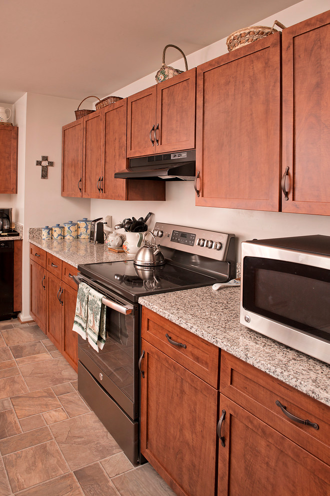 Rustik inredning av ett u-kök, med en undermonterad diskho, luckor med infälld panel, skåp i mellenmörkt trä, laminatbänkskiva, svarta vitvaror och en köksö