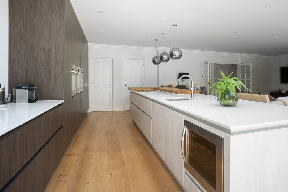 Inspiration for a large contemporary galley open plan kitchen in Essex with an integrated sink, flat-panel cabinets, brown cabinets, quartz worktops, integrated appliances, medium hardwood flooring, an island, brown floors and white worktops.