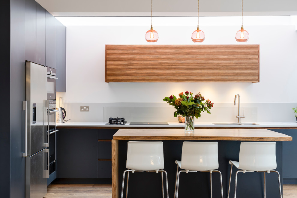 This is an example of a contemporary l-shaped kitchen in London with a double-bowl sink, flat-panel cabinets, blue cabinets, stainless steel appliances, light hardwood flooring and an island.