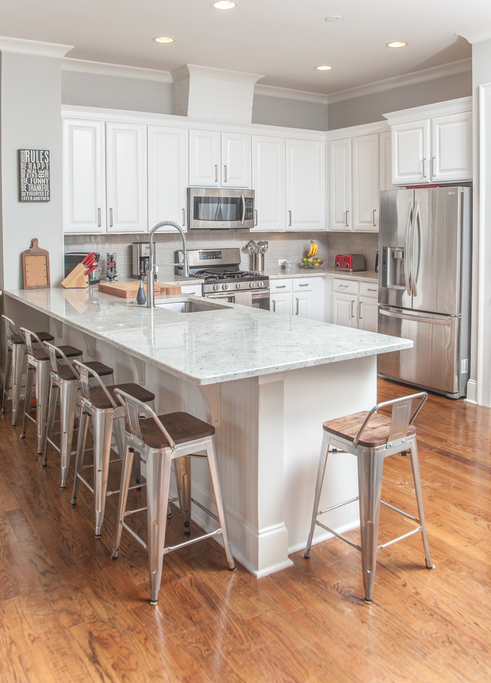 Example of a mid-sized trendy l-shaped light wood floor eat-in kitchen design in Atlanta with a single-bowl sink, white cabinets, granite countertops, gray backsplash, ceramic backsplash and a peninsula