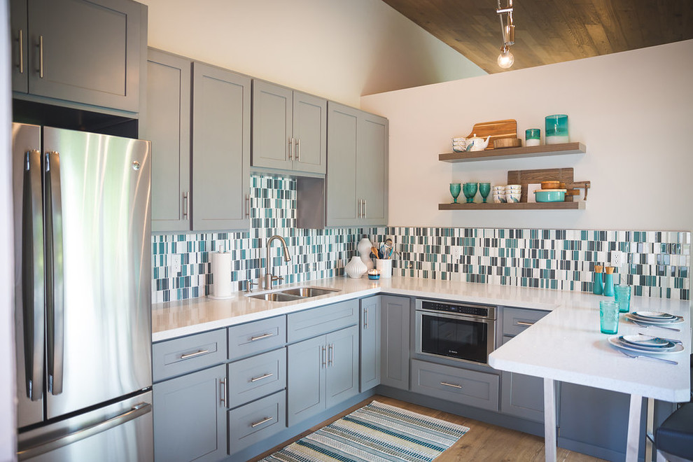 Exempel på ett mellanstort modernt kök, med en undermonterad diskho, skåp i shakerstil, grå skåp, bänkskiva i kvartsit, blått stänkskydd, stänkskydd i mosaik, rostfria vitvaror, ljust trägolv, en halv köksö och grått golv