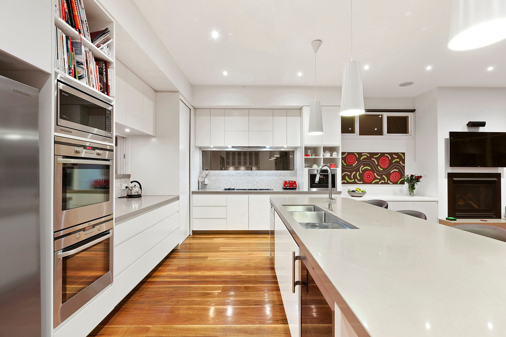 Immagine di una cucina design di medie dimensioni con lavello sottopiano, ante lisce, ante bianche, elettrodomestici in acciaio inossidabile e pavimento in legno massello medio