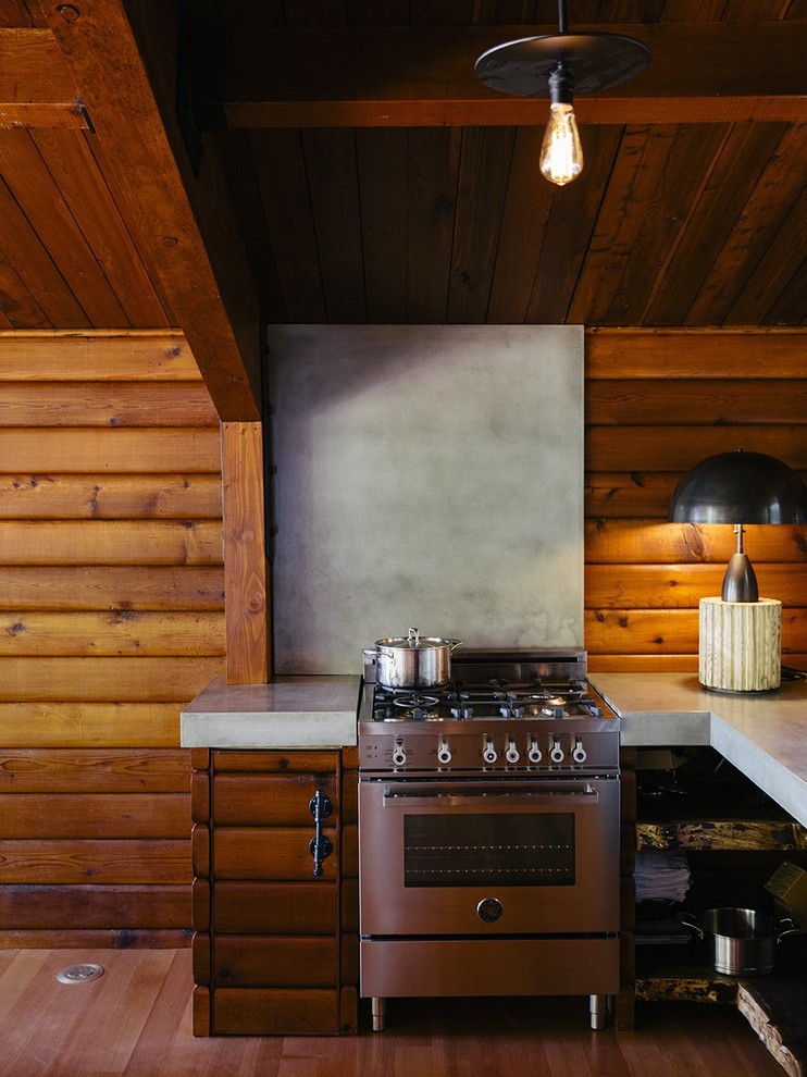 Diseño de cocinas en L rústica pequeña con puertas de armario de madera oscura, encimera de cemento, salpicadero verde, electrodomésticos de acero inoxidable y suelo de madera clara