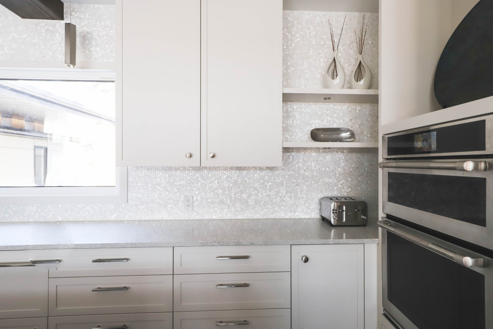 Inredning av ett klassiskt kök med öppen planlösning, med en undermonterad diskho, skåp i shakerstil, vita skåp, bänkskiva i kvartsit, vitt stänkskydd, stänkskydd i mosaik, rostfria vitvaror, vinylgolv och en köksö