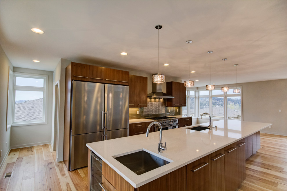 Large trendy galley bamboo floor and beige floor eat-in kitchen photo in Seattle with flat-panel cabinets, dark wood cabinets, solid surface countertops, green backsplash, glass tile backsplash, an island, an undermount sink and stainless steel appliances