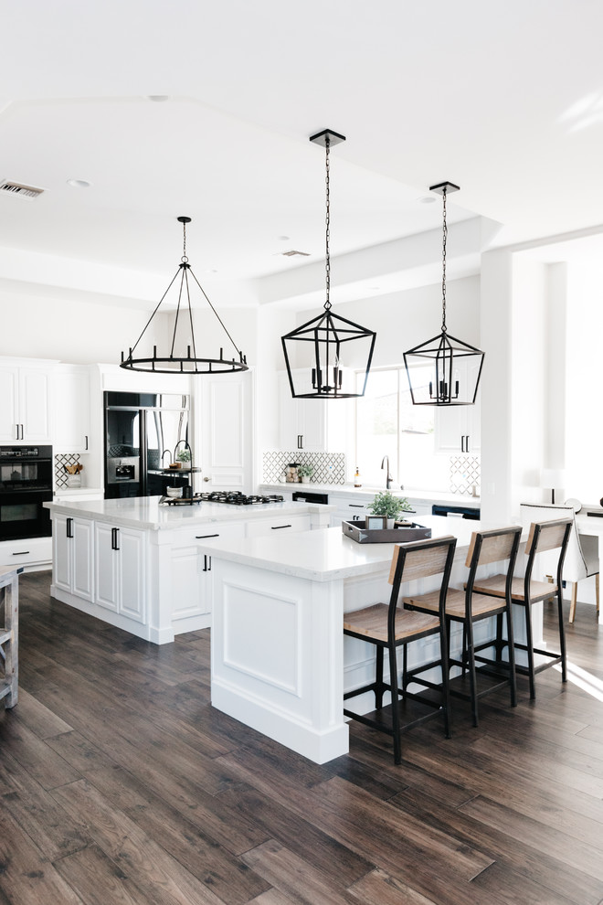 Inspiration for a traditional kitchen in Phoenix with a submerged sink, white cabinets, engineered stone countertops, black splashback, marble splashback, black appliances, medium hardwood flooring, multiple islands, brown floors and white worktops.