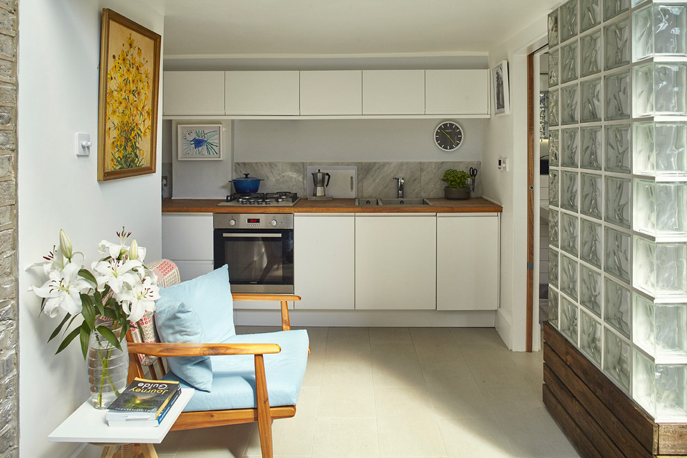 Photo of a small contemporary single-wall kitchen in London with a double-bowl sink, flat-panel cabinets, white cabinets and stainless steel appliances.